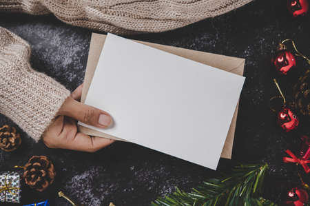 Hands holding opened card or letter. Blank cover Mock-up. With ribbons, gift boxes and dried pine...