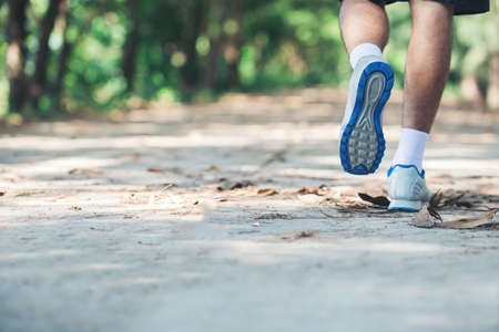 close up foot of young runner man running along road in the park.