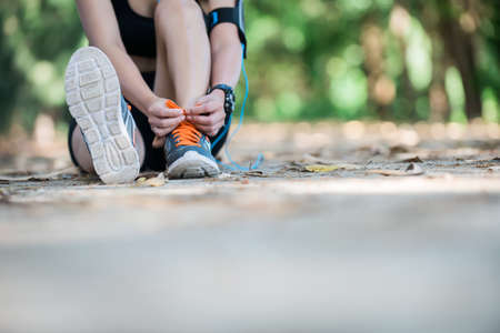 Young beautiful girl athlete with armband and earphones listening to music and tying laces on her...