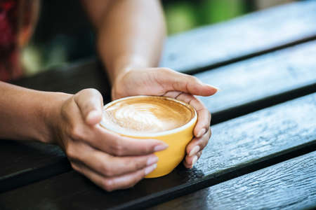 Woman's hands holding cup of coffee at cafeの写真素材