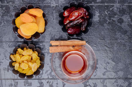 top view of dried fruits raisins apricots and dried dates in mini tart tins served with tea on black wooden backgroundの写真素材