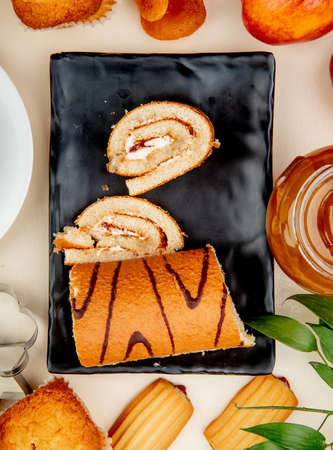 top view of cut and sliced roll in plate with jam cupcake cookies peach around on white background