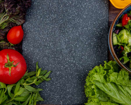top view of cut and whole vegetables as tomato basil mint cucumber lettuce with cutting board as backgroundの写真素材