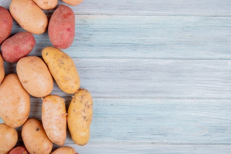 top view of russet white yellow and red potatoes on left side and wooden background with copy spaceの写真素材