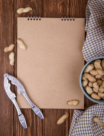 top view of sketchbook and a bowl filled with peanuts in shell and nut cracker on wooden backgroundの写真素材