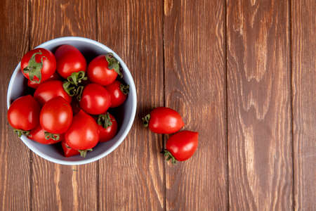 top view of tomatoes in bowl with other ones on left side and wooden background with copy spaceの写真素材