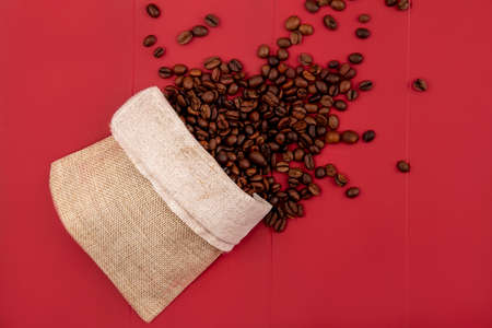 top view of fresh roasted coffee beans falling out of a burlap bag on a red backgroundの写真素材