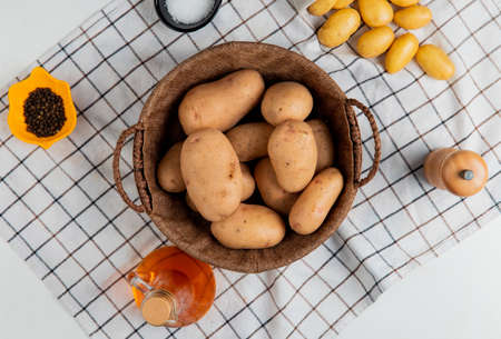 top view of potatoes in basket with butter salt black pepper on plaid cloth and white background