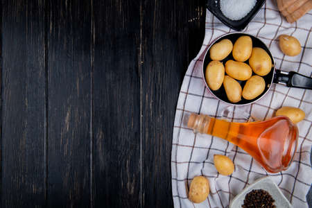 top view of potatoes in pan with salt melted butter black pepper seeds on plaid cloth and wooden background with copy spaceの写真素材