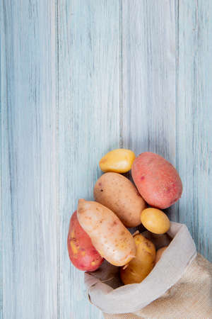 top view of new russet and red potatoes spilling out of sack on wooden background with copy spaceの写真素材
