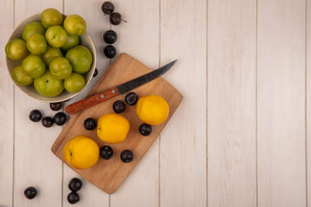 top view of green cherry plums on a bowl with yellow peaches on a wooden kitchen board with knife with sloes on a grey wooden background with copy spaceの写真素材