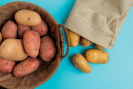 top view of potatoes in basket and other ones spilling out of sack on blue backgroundの写真素材