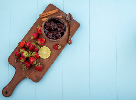 top view of fresh strawberry on a wooden kitchen board with a strawberry jam with a slice of lime on a blue background with copy spaceの写真素材