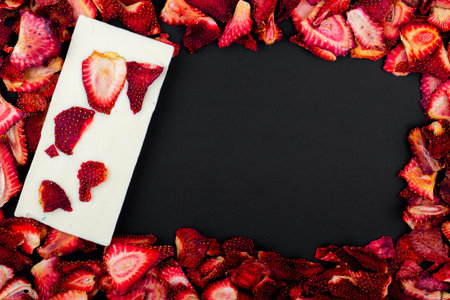 top view of dried strawberry slices with white chocolate bar on black background
