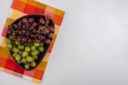 top view of grapes in bowl on plaid cloth on white background with copy spaceの写真素材