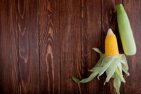 top view of corn cobs with shell on wooden background with copy space