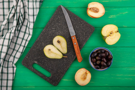 top view of half cut pear and knife on cutting board with plaid cloth and half cut peach and apple...