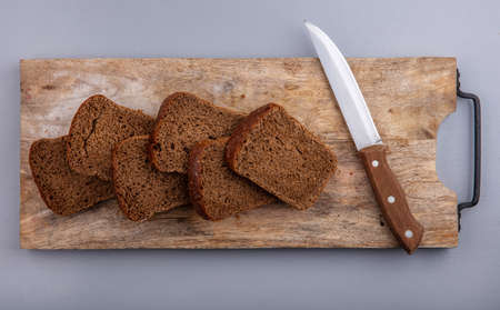 top view of sliced rye bread and knife on cutting board on gray background