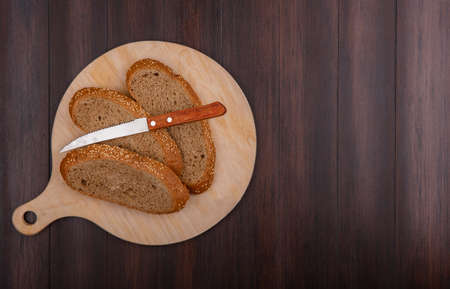 top view of sliced seeded brown cob with knife on cutting board on wooden background with copy spaceの写真素材