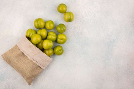 top view of green plums spilling out of sack on white background with copy spaceの写真素材