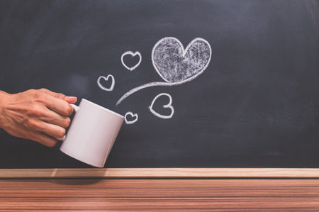 The hand holds the coffee cup and the heart shape is on the blackboardの素材