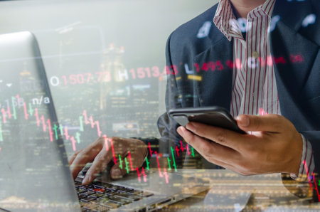 Businessman hands use mobile phones and computers to view stock information on the Internet.の素材