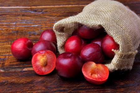 raw and fresh organic plums inside rustic fabric bag on wooden table. Close-up view.の素材