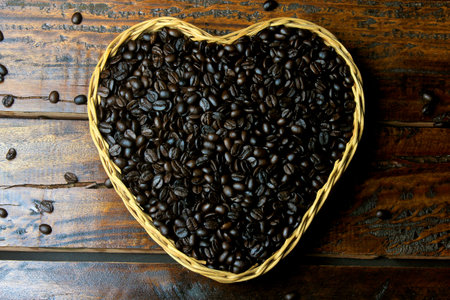 roasted coffee beans inside basket with heart shape on rustic wooden table. Top viewの素材