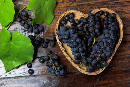 bunches of grape inside basket with heart shape on wooden table, top viewの素材