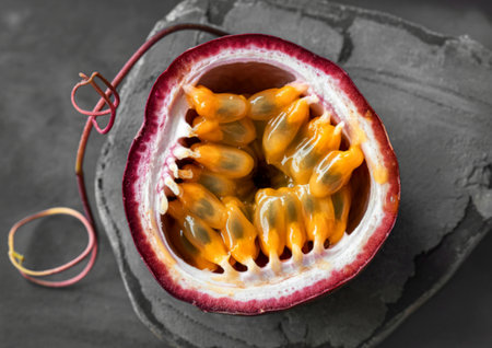 A close-up, overhead view of a ripe passion fruit cut in half, showcasing its bright yellow,...