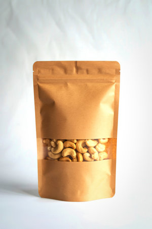 A front view of a resealable brown kraft paper pouch showcasing a clear window filled with roasted cashews against a white background.の写真素材