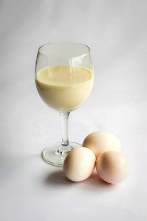 A glass of creamy egg liqueur sits next to a few whole eggs, suggesting a homemade or artisanal beverage.の写真素材
