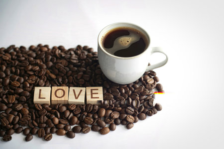 A white mug filled with dark coffee sits atop a bed of roasted coffee beans. Wooden letter blocks spell out the word LOVE.の写真素材