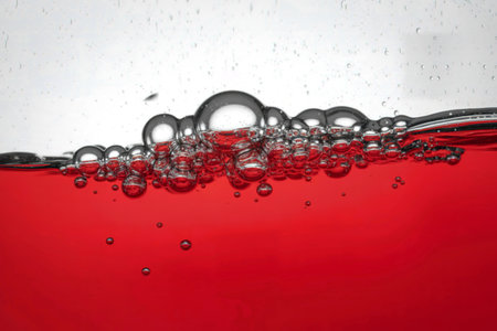 Macro shot of a vibrant red liquid with a stream of clear bubbles rising to the surface against a clean white backdrop.の写真素材
