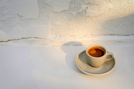 A single cup of steaming espresso sits on a saucer, bathed in soft, natural light with subtle shadows.の写真素材