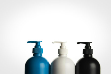 Three pump bottles, one teal, one off-white, and one black, stand in a row against a clean white backdrop.の写真素材
