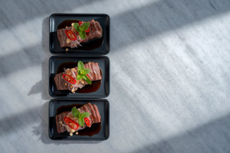 Three small black square dishes are stacked vertically, each containing a portion of sliced meat...