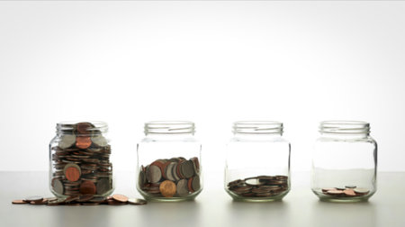 Four glass jars lined up, each containing a different amount of coins, illustrating progressive...