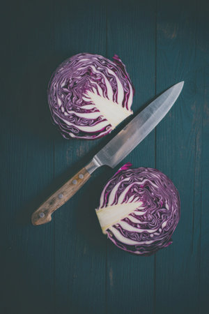 A close-up image of sliced red cabbage with a knife on a dark wooden surface.