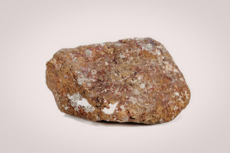 A brown rock with red and white specks is shown on a white background. The rock has a rough texture...