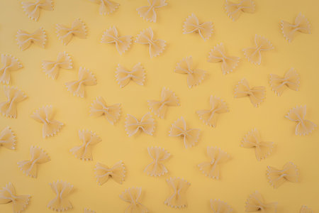 A collection of bow tie pasta arranged on a bright yellow background, showcasing the food's texture...
