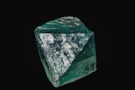 A close-up image of a rough emerald gemstone with a predominantly green color and white inclusions,...