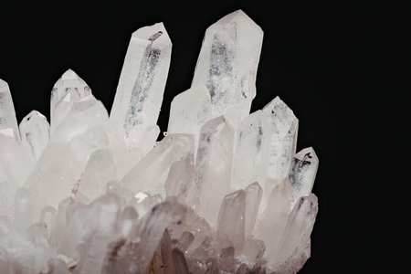 This image features a cluster of clear quartz crystals with pointed tips, set against a black...