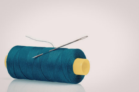 A spool of blue thread with a needle on top, isolated on a white background.