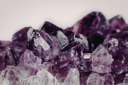 A close-up view of a pile of raw amethyst gemstones on a white background, showcasing their deep purple color and crystalline structure.の写真素材