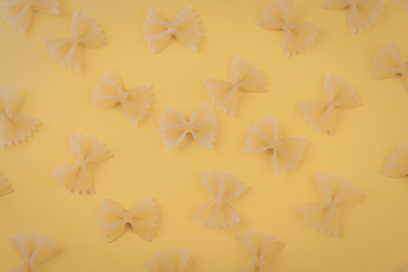 A collection of bow tie pasta pieces arranged on a bright yellow surface