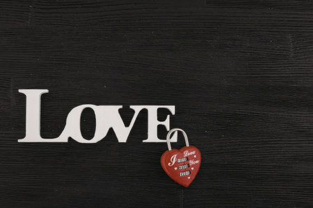 A red heart shaped padlock hanging from the letter E in the word LOVE on a black wooden background