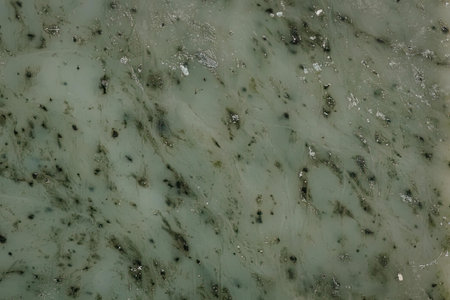 A close-up view of a green marble surface featuring black spots and a smooth texture, showcasing its...