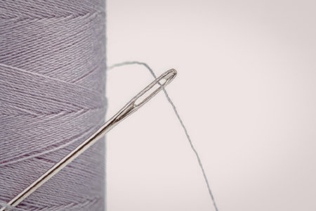 A spool of purple thread with a sewing needle threaded through it.
