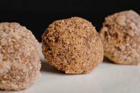 Three brown coconut balls on a white surface with a black background, likely a food item.